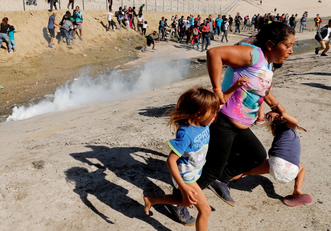 A migrant family runs away from tear gas in front of the border wall between the U.S and Mexico, in Tijuana